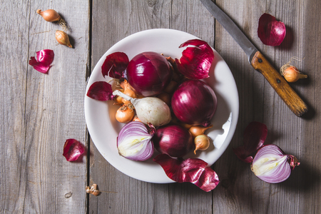 Several kinds of different onion bulbs at a white plate, standing on an old wooden table. Above view still lifeの写真素材