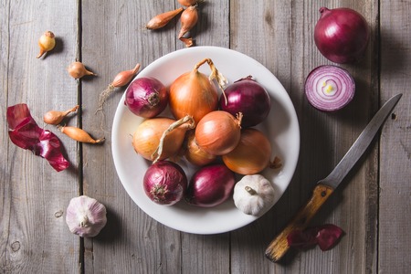 Several kinds of different onion bulbs at a white plate, standing on an old wooden table. Above view still lifeの写真素材