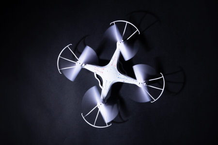 Photo of white quadrocopter on black background. Above view