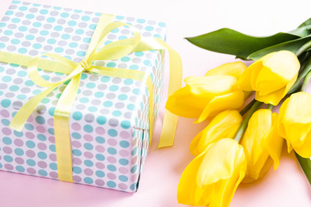 Bouquet of beautiful fresh yellow tulips on pink background and gifg box. View from above photo
