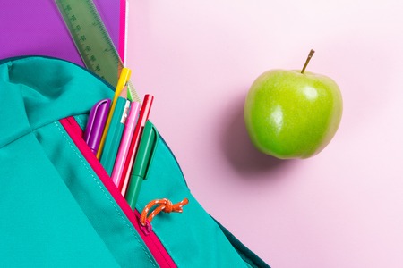 Backpack with school stationery and apple on pink backgroundの写真素材