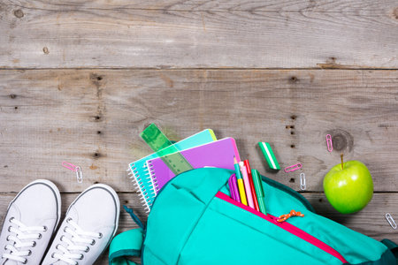 Backpack with school stationery and apple on wooden background
