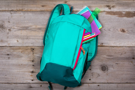 Backpack with school stationery and apple on wooden background