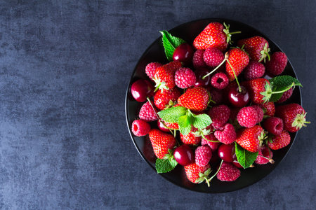 Fresh red ripe berries on black plate. Top view, copy space