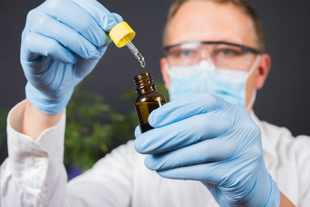 Portrait of scientist with mask, glasses and gloves researching and examining hemp oil in a...