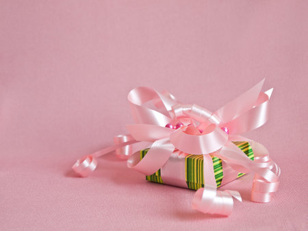 Green gift box with pink ribbon and bow on the pink background.の写真素材