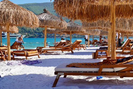 Bodrum, Turkey - August, 2020: Snow-white beach of Lux Hotel with emerald water of Aegean Sea. Yachts.People sunbathing on the beach. Sunbeds on the beach. Relaxing Deluxe Leisure Conceptionのeditorial素材
