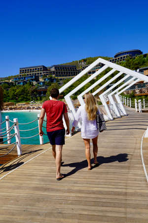 Bodrum, Turkey - August, 2020: Young beautiful people on the beach with emerald clear water walk on a wooden deck on the beach. luxury Lujo hotelのeditorial素材