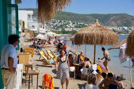 Bodrum, Turkey - August, 2020: Lots of people on the beach of Kumbahce Bay. Bodrum, Mugla province, Turkey. People sunbathe, have lunch at a cafe, walk on the beach.のeditorial素材