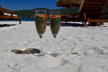 Two cold glasses of champagne with raspberry on white sand on the beach in an emerald bay. Luxury resort with sea view. Romantic vacationの写真素材