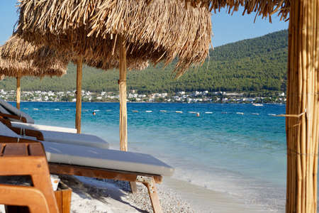 Bodrum, Turkey - August, 2020 A pearl of the Aegean sea with beaches and coasts suitable for unforgettable sea holidays. Holiday banner. Hotel Lux Lujo beach at sunrise. Bamboo parasols, azure ocean, white boats, green covered hills, white sands and blue sky. Amazing viewの写真素材