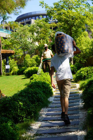 Bodrum, Turkey - August, 2020 Adult man in hat is holding a water hose and watering his garden. Work in the house and garden, care for the territory. Service staff at the hotelのeditorial素材