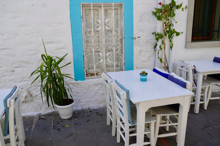 Bodrum, Turkey - August, 2020: Authentic Streets of Bodrum by the Sea. Blue window, white tables on the street. Traditional Mediterranean cafe. Cozy street cafe near the beautiful Aegean Sea.のeditorial素材