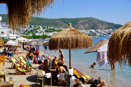Bodrum, Turkey - August, 2020: Lots of people on the beach of Kumbahce Bay. Bodrum, Mugla province, Turkey. People sunbathe, have lunch at a cafe, walk on the beach.のeditorial素材