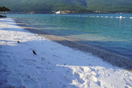 Snow white sand and pebbles on the ocean coast near the emerald ocean at sunset Slice of paradiseの写真素材