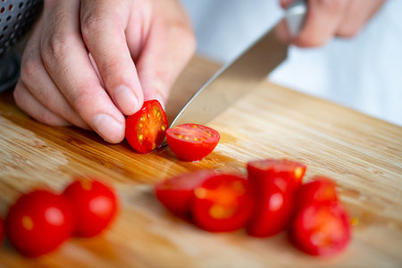 Man slicing cherry tomatoes on cutting board.の写真素材