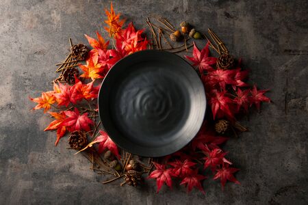 Autumn frame with artificial red maple leaves and empty black plate.の写真素材