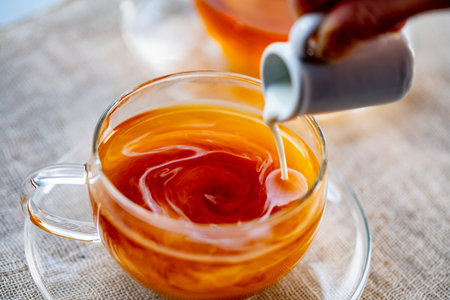 Pouring milk into cup with aromatic tea.