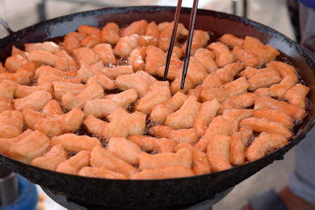 Many deep-fried doughstick are in a large iron pan, With boiling oil.の写真素材