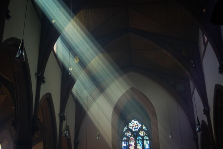 Seeing the light, shafts of sunshine stream through stained glass window into historic churchの写真素材