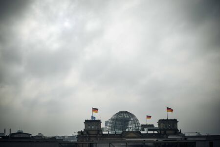 building of the German Bundestag in Berlin from outside with flags under cloudy, gloomy sky and bad weatherの写真素材