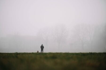 man and his dog waiting on meadow in misty atmosphereの写真素材