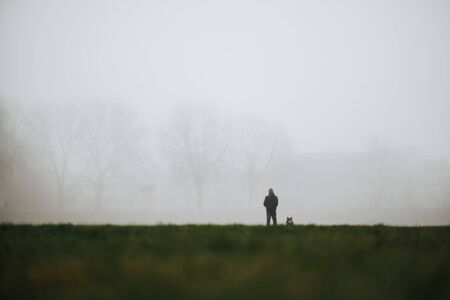 man and his dog as symbol of loyal friendship waiting in fogの写真素材