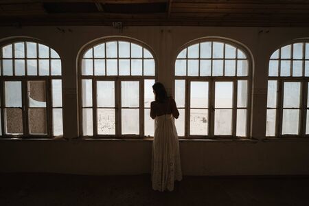 bride looking outside windows of an old colonial villaの写真素材