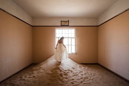 young woman in abandoned desert house enjoying playing with white dressの写真素材