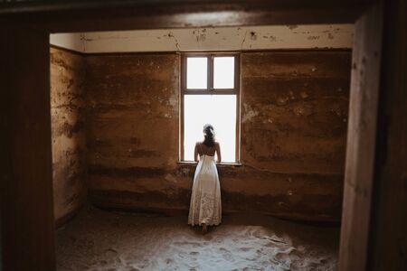 bride looking through window of old desert house on her wedding dayの写真素材