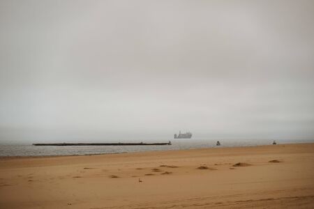 shore coast with oil tankers on the sea in bad weather with stormy cloudsの写真素材