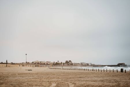 Swakopmund Promenade at the Beach and Coast along the South Atlantic Ocean under cloudy sky. Large Desert Dunes behind visible on the horizon. South Atlantic Ocean, Erongo Region, Namibia, Africaの写真素材