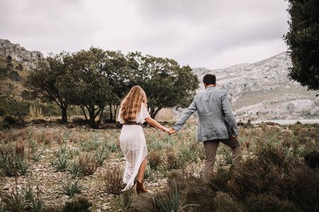 bride and groom walking in nature, holding hands and smiling at each other in a horizontal full length shotの写真素材