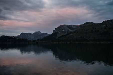 Beautiful landscape with high mountains with illuminated peaks, stones in mountain lake, reflection, blue sky and yellow sunlight in sunrise. Amazing scene, Spain, Europe April 2019の写真素材