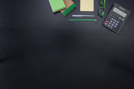 Green, black, yellow office desk business background with post it, goggles, notepad, calculator, pencil and penの写真素材