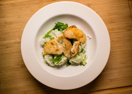 Baked chicken dish with parmesan, spinach and rice on a wooden chopping boardの写真素材