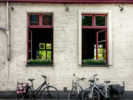 Cute bikes parked against the white bricked wall of a tavern with open windows, red frames, flowers in them. Location: Belgiumの写真素材