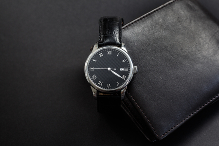 Close-up of a Luxury Black Wristwratch. An elegant, stylish black automatic watch with a black leather wallet on a dark gray background.の写真素材