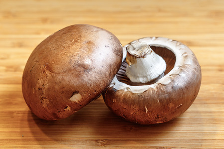 Two commonly used mushrooms, agaricus bisporus, on a wooden chopping boardの写真素材