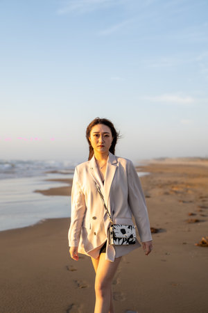 Beautiful young brunette woman in a white coat walking on the beachの写真素材