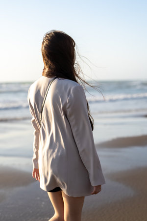 Back view of a young woman walking on the beach in the morningの写真素材