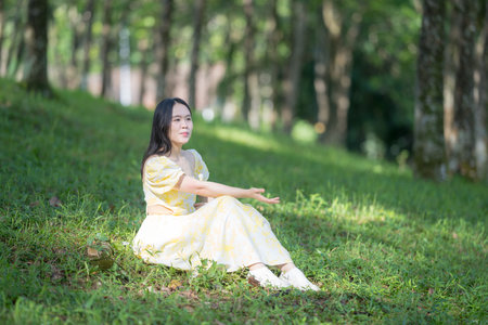 Twenty-something Chinese woman in yellow dress gracefully playing violin in the forest of a large, nature-filled park in Bukit Jalil, near Kuala Lumpur, Malaysia.の写真素材