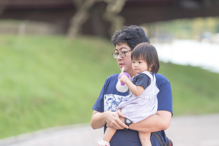 A one-year-old Chinese Malaysian girl playing on the children's playground equipment with her thirty-something father at KLCC Park in Kuala Lumpur City Centre, Malaysia.の写真素材