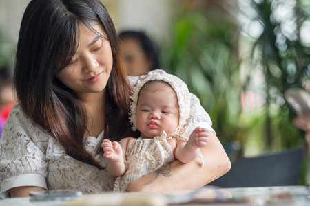 A twenty-something Malaysian woman holding a few-months-old baby at a stylish cafe in Selangor,...