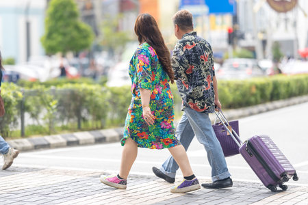50-something Malay man and 30-something Chinese woman in colorful clothes walking together with suitcases near a train station in Kuala Lumpur, Malaysia.の写真素材