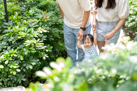 A 1 year old Taiwanese girl walking hand in hand with her parents, a man and woman in their 20s, on a hot sunny day in the streets of Taichung City, Taiwan, in September.の写真素材