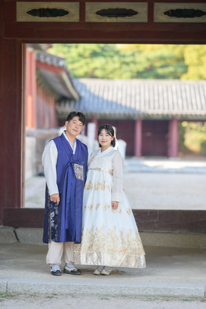 A Korean couple in their 30s and a woman in their 20s stand together in front of a historical building in Seoul, South Korea, wearing Hanbok.の写真素材