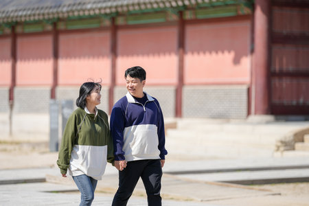 A sporty Korean couple, a man in his 30s and a woman in her 20s, wearing tracksuits, spends their time together happily at a historical building in Seoul, South Korea.の写真素材