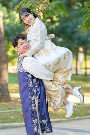 A Korean couple, a man in his 30s and a woman in her 20s, are wearing Hanbok and hugging each other in a park surrounded by green trees in Seoul, South Korea.の写真素材