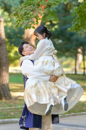 A Korean couple, a man in his 30s and a woman in her 20s, are wearing Hanbok and hugging each other in a park surrounded by green trees in Seoul, South Korea.の写真素材